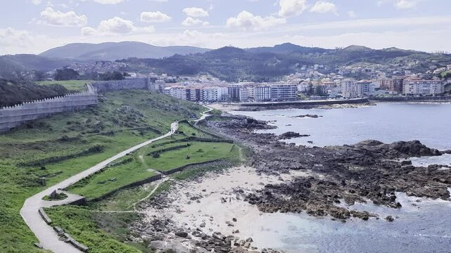 A sweeping view highlights Baiona's Monterreal Castle and its stunning coastal landscape in Galicia, Spain. It reveals ancient walls, rugged shores, and a picturesque town, embodying Iberian heritage.