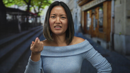 Young woman standing on a city street with a serious expression, wearing a blue top, showcasing...