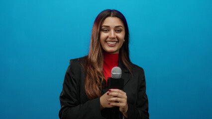 Hispanic woman reporter smiling confidently while holding a microphone against a vibrant blue...
