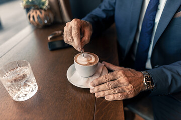 Senior Businessman Stirring Cappuccino at a Café Table, Cozy Atmosphere