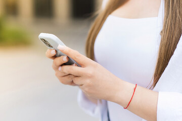 Close-up of a young woman's hands using a mobile phone while walking outdoors in the city....