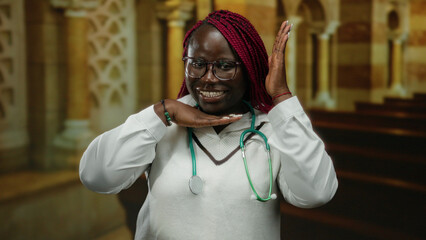 Confident woman with stethoscope smiling indoors at church setting, making framing gesture with...