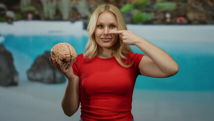 Woman in red shirt holding brain by pool in hotel scenario, touching her nose with a thoughtful...