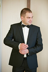 A man in a black suit and white shirt is getting ready for a formal event. He is adjusting his tie...
