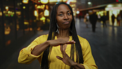 Woman gesturing on an urban street at night wearing a yellow shirt with braids visible in a city...