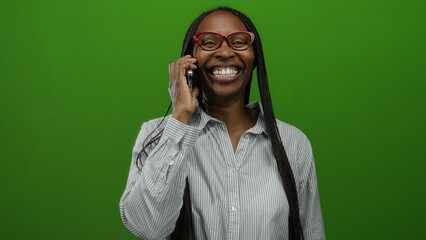 Woman laughing while talking on cellphone against isolated green background showcasing joyful...