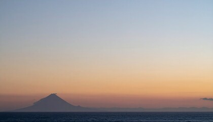 火山の山影が静かに佇み、右側には柔らかな夕焼け色が広がるマットな空が大きく開け、滑らかなグラデーションで穏やかな時間を描く風景写真
