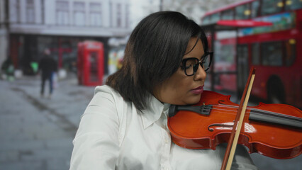 Woman playing violin on street with focus on young hispanic musician in urban city outdoor setting...
