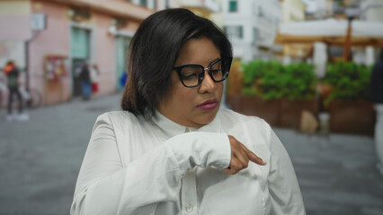 Latin plus-size woman with glasses gestures thoughtfully on a vibrant city street, showcasing...