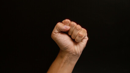 Man raising clenched fist against a black background signifies strength, protest, resistance, and empowerment in a striking, focused composition