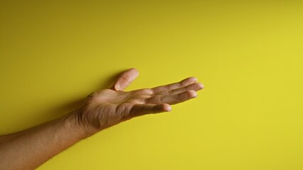 Man extending hand with fingers spread against a vibrant yellow background showcasing a gesture of...