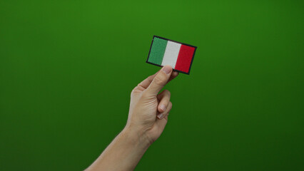 Male hand holding italian flag embroidery against a vibrant green background, symbolizing italy's...