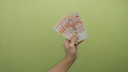 Man holding singapore dollars against a yellow background, showcasing a fan of banknotes with an...