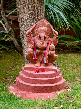 Statue of Lord Ganesha in pink stone established in the garden and adorned with flowers