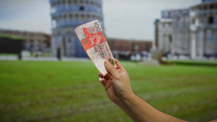 Man holding hong kong dollars in front of pisa's leaning tower, highlighting international currency and travel in an urban italian setting outdoors in the city.