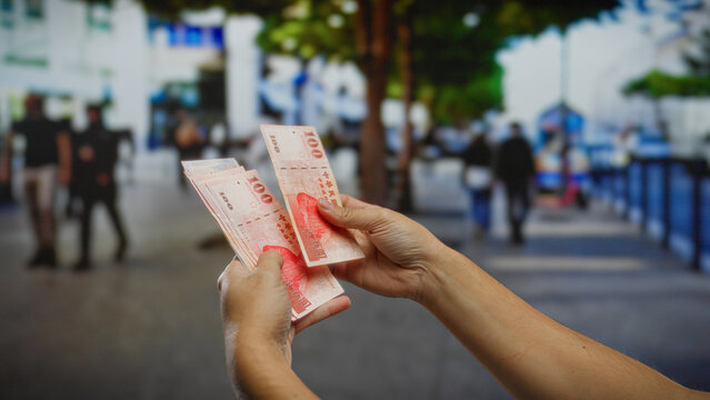 Hands holding taiwanese dollars on a busy urban street, capturing the essence of outdoor business and financial transactions amid city life.