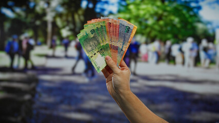 Hand holding south african rand banknotes with urban street and people in the background, capturing...