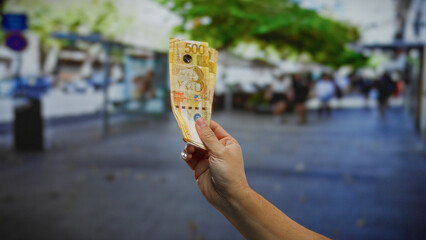 Hand holding philippine pesos outdoors on a city street, symbolizing money, business, and...