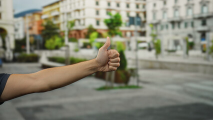 Man giving thumbs up with focus on hand and arm in an urban street setting during daytime...