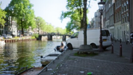 Blurred view of amsterdam canal with defocused background showing a white van and a boat on a sunny day.