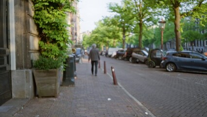 Man walking down a blurred european street with cars and trees lining the cobblestone pavement on a...
