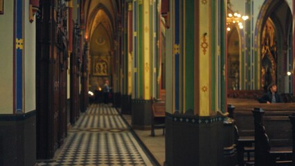 Blurry interior of a catholic church with colorful columns and defocused people adding to the...