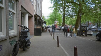 Obraz premium Blurred street scene with people walking on a european city sidewalk, showcasing urban life, bokeh effect, and defocused background, trees and bicycles visible.