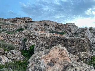 Fototapeta premium Rocky limestone terrain with sparse vegetation under a partly cloudy sky