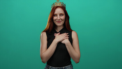 Woman with crown standing against vibrant green background with hands placed over her chest,...