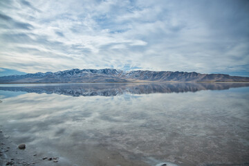 Vibrant autumn-sky hues paint the shoreline of Utah’s Great Salt Lake. Calm blue waters mirror cotton‑cloud skies, while distant mountains stand quietly, embracing seasonal wonder.