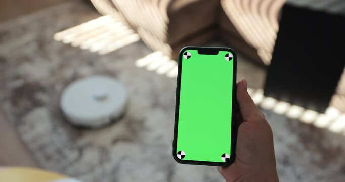 Robot vacuum cleaner performs automatic cleaning of the house at a certain time. Woman using mobile phone with green screen in living room. Green screen chroma key. Smart home concept.