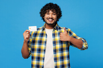 Young happy Indian man he wear yellow checkered shirt casual clothes hold in hand mock up of credit...