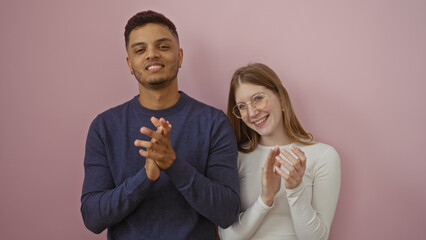 Man and woman clapping joyfully on a pink background, symbolizing a happy, supportive relationship...