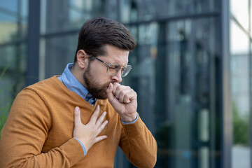 Close-up photo of a young man sitting on a bench outside an office, holding his hand to his chest,...