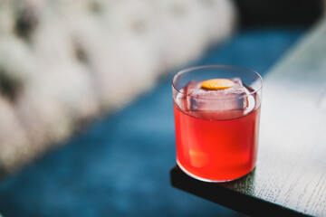 Close-up of a red cocktail with ice and orange peel garnish in a clear glass on dark wooden table,...