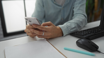 Man in office holding smartphone surrounded by keyboard mouse papers illustrating productive work environment with a modern tech-savvy appeal