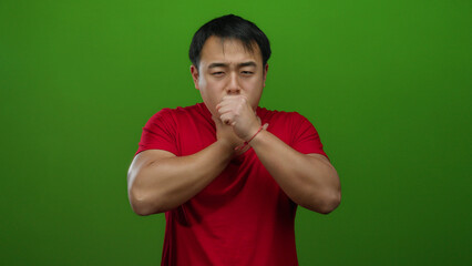 Young man in a red shirt with sore throat on green background looking uncomfortable and pained,...