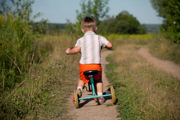 Boy rides a tricycle on a country road in summer.