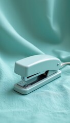 Mint Green Metal Stapler on Soft Blue Fabric Background
