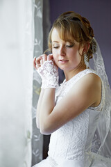 A woman in a white wedding dress is looking at her hands. She is wearing a veil and has her hands...