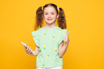 Little smiling cute kid child girl 8-9 years old wears green t-shirt hold in hand use mobile cell...
