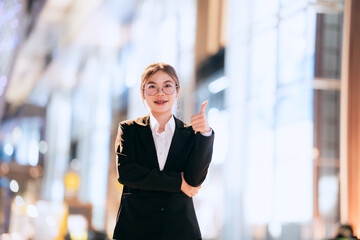 Confident young businesswoman in a black suit standing outdoors at night, smiling with arms...