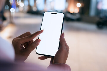 A close-up of a woman using a smartphone with a blank white screen at night. Technology, communication, and digital interaction in a modern urban setting.