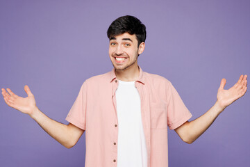 Young sad shocked man he wears pink shirt t-shirt casual clothes shrugging shoulders looking...