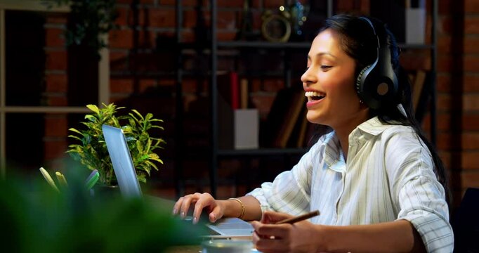 Indian businesswoman smiling attending video call on laptop using headphone at desk in modern cozy office, Asian young corporate executive expressing positivity while engaged in virtual meeting - Powered by Adobe