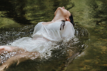 A young woman dressed in white enjoys relaxing in a calm river surrounded by nature. The peaceful...