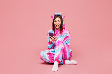 Full body young fun woman she wear domestic costume with hoody and animal ears sit hold in hand use mobile cell phone isolated on plain pastel light pink background studio portrait. Lifestyle concept.