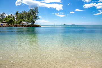 Klong Prao Beach's turquoise channel separating from Kai Bae Beach, with palm-fringed cape and bungalows on opposite shore under sunny skies. Koh Chang, Thailand.

