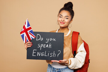 Young smart girl student wears casual clothes backpack bag hold British flag card with Do you speak...