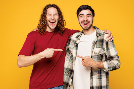 Young smiling two friends buddies men they wear casual clothes together point index finger on each other look camera isolated on plain yellow orange color background studio portrait Lifestyle concept